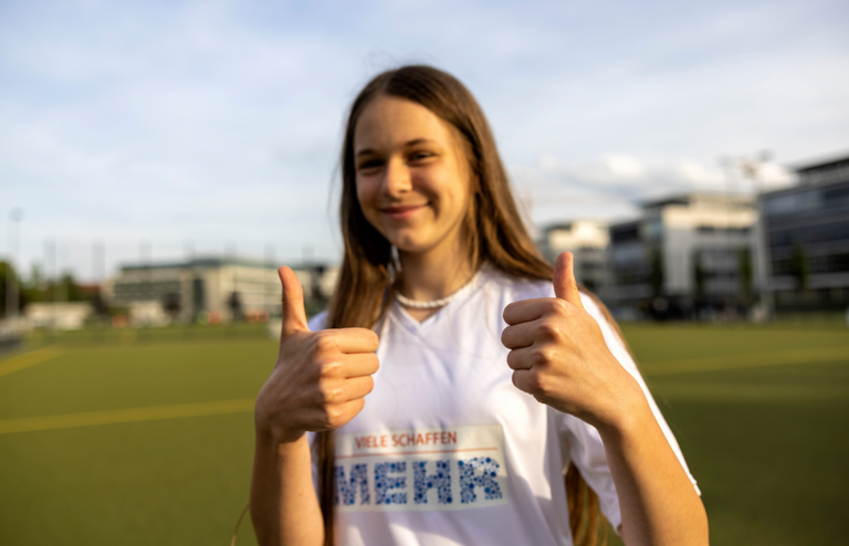 Bild mit Mädchen im Viele schaffen Mehr T-Shirt. Daumane nach oben.